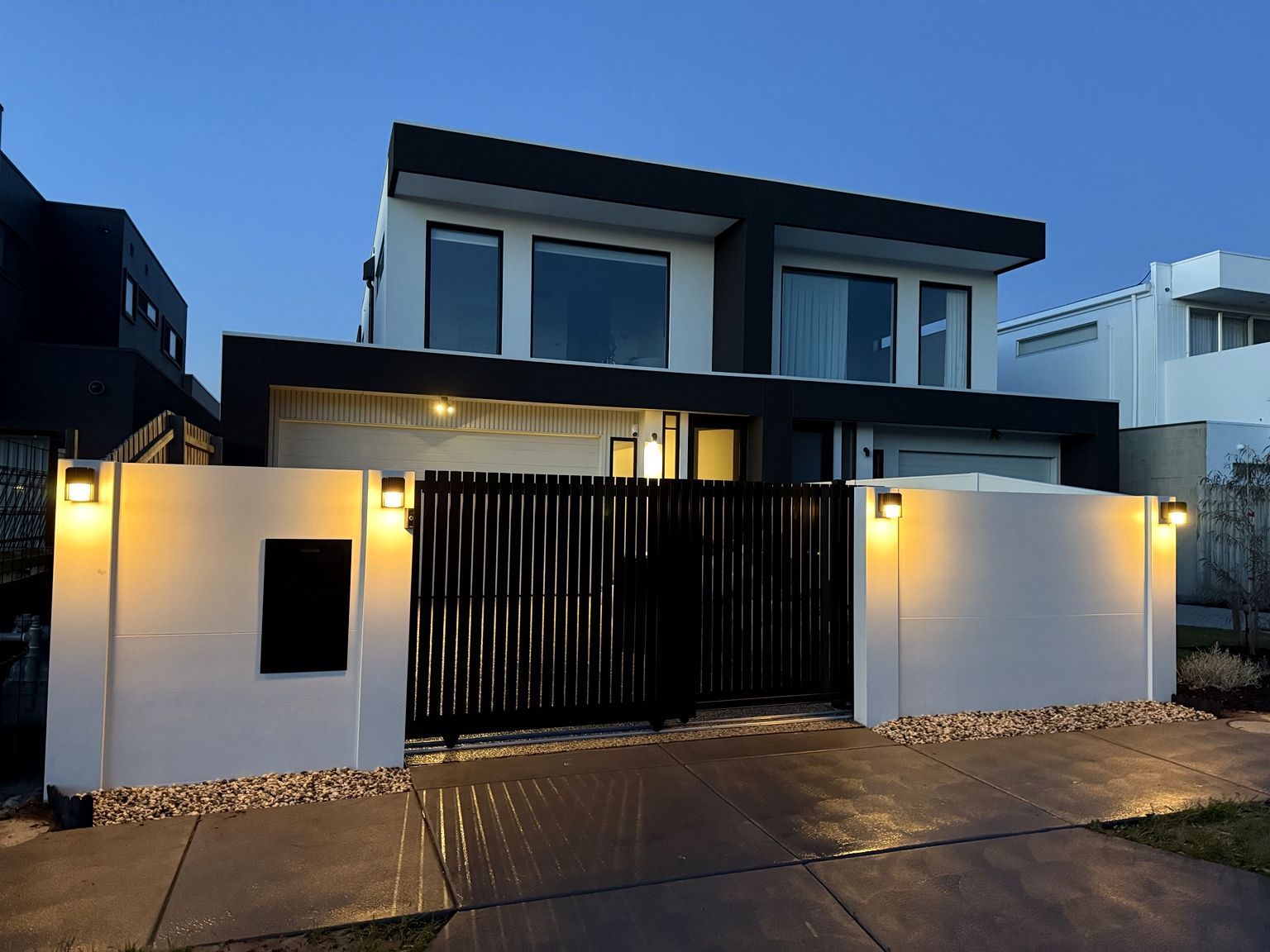 Chelsea frontage at dusk: rendered wall, lit posts and a dark automated gate.