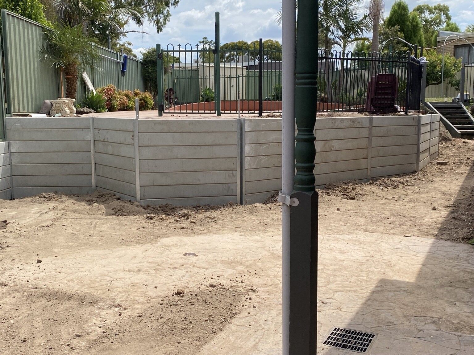 A curved concrete sleeper retaining wall on steel posts below a pool terrace, Endeavour Hills, before the site was cleaned up.