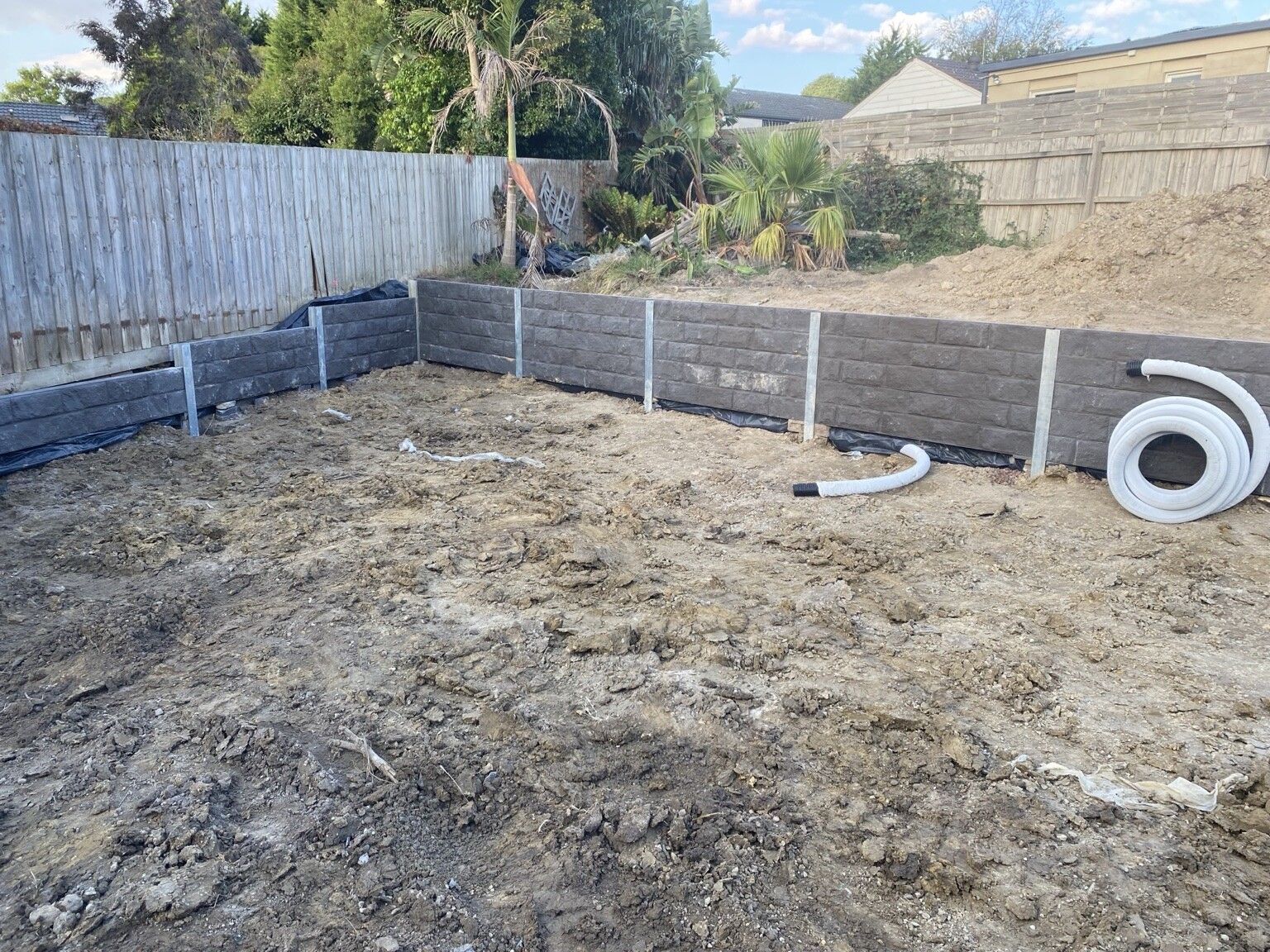 Stepped concrete sleeper walls at Frankston South during construction, with membrane at the base and a coil of drainage pipe on the soil.