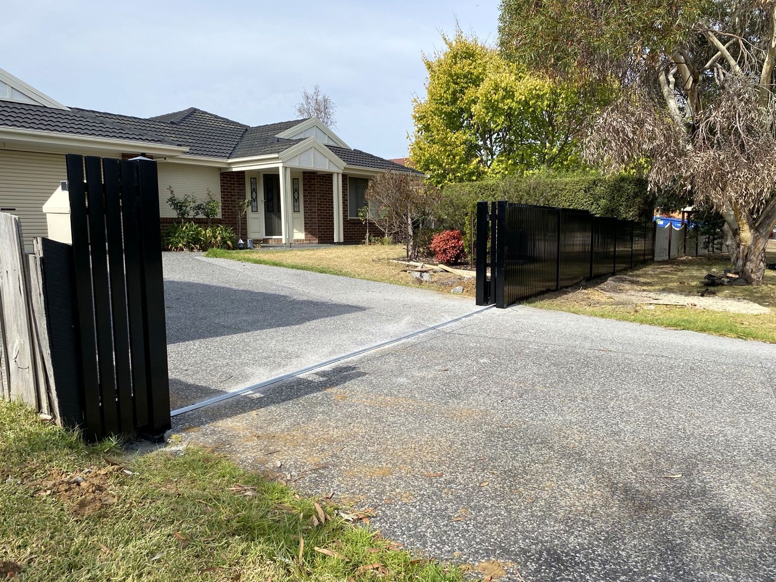 Mornington: the black aluminium blade sliding gate slid back beside the matching blade fence, leaving the driveway clear, with the gate track running across it.