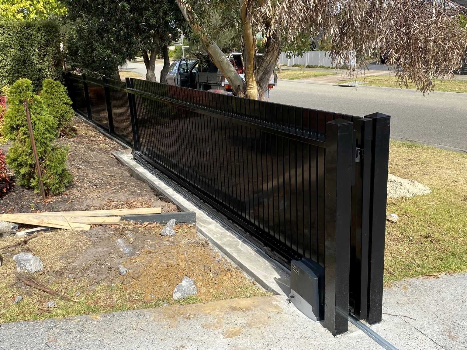 A black aluminium blade sliding gate on its track at Mornington, with the gate motor at the foot of the end post.