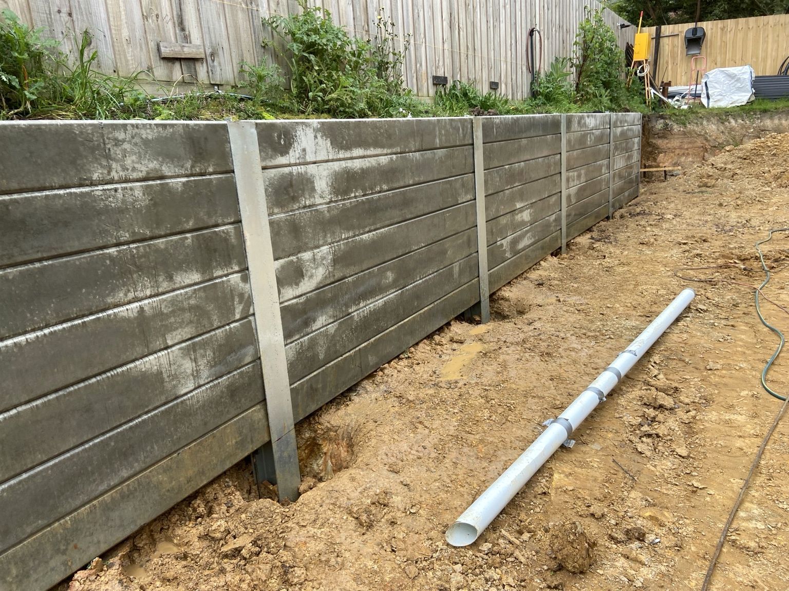 Concrete sleepers between steel posts on the Mount Eliza wall, with a length of pipe on the ground in front.