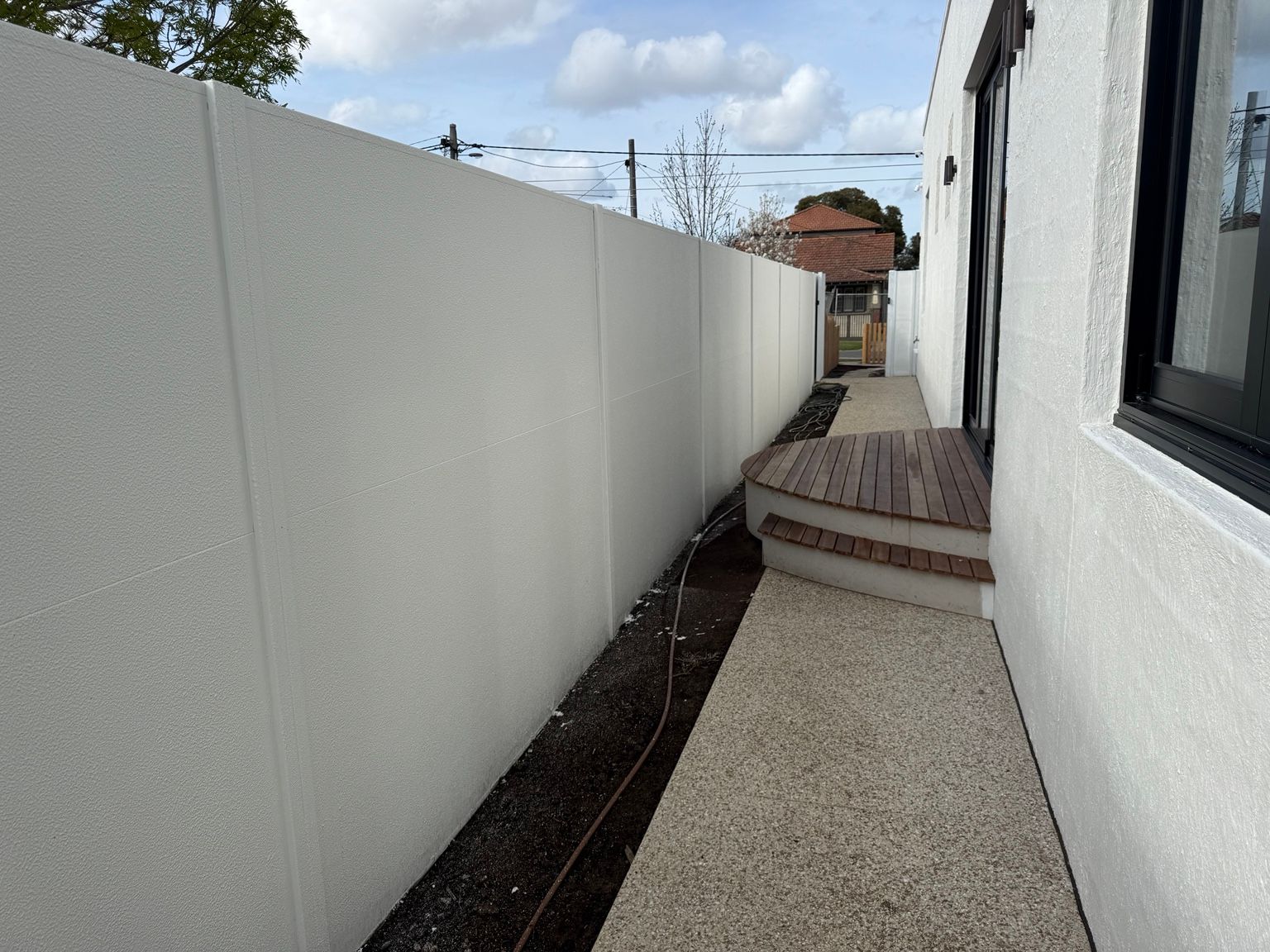 A white SlimWall side boundary running beside a house and a timber deck, Reservoir.